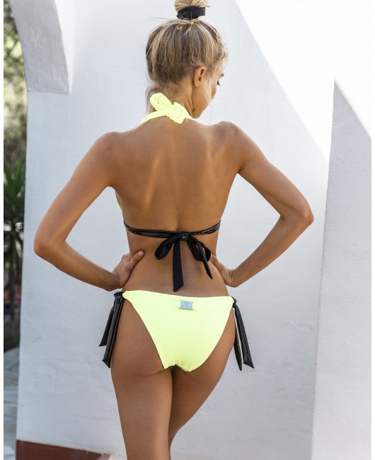 Eine Frau mit blondem Haar in einem Dutt modelliert einen neongelben Bikini von Eniqua und posiert mit dem Rücken zur Kamera.